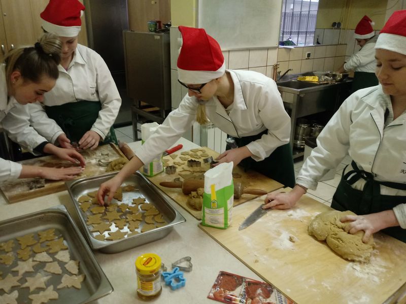 Pięć uczennic w mikołajowych czapkach przygotowuje świąteczne pierniczki w kształcie gwiazdek, choinek i księżyców